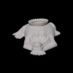 May include: A white ceramic alligator-shaped planter with a scalloped rim. The alligator is lying down with its legs outstretched, and its eyes are wide open. The planter is a decorative item.