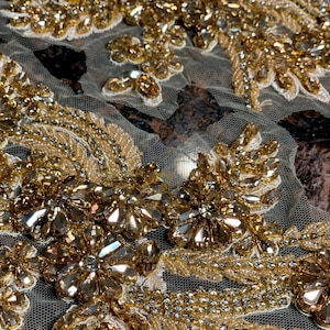 Op de afbeelding: Gouden kralen- en paillettenapplicatie met een bloemenmotief op een transparante stof.