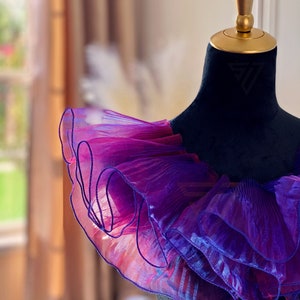 May include: A purple and pink ruffled collar made of sheer fabric. The collar is on a black dress form.
