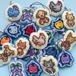 Puede incluir: Una colección de 18 llaveros de fieltro coloridos con varios diseños de animales y plantas. Los llaveros están cosidos a mano y tienen un estilo caprichoso y pixelado.