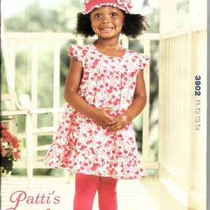 May include: A sewing pattern for a toddler's pinafore dress and leggings. The pattern is called "Patti's Pinafore" and is from Kwik Sew by Kerstin Martensson. The pattern number is 3902. The model is wearing a pink and white floral dress with a ruffled hem and pink leggings. She is also wearing a white hat with a pink ribbon.