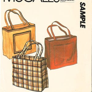 May include: McCall's pattern cover featuring illustrations of three tote bags. One is a solid orange with a rectangular accent, another is a solid brown with a pocket, and the third is a plaid pattern. The word "SAMPLE" is printed vertically.