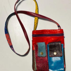 May include: A multi-colored leather crossbody bag with a long strap. The bag has a red, blue, brown, and purple patchwork design with a zipper closure.