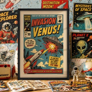 May include: A framed vintage-style comic book cover titled Invasion from Venus! featuring a rocket ship firing at a flying saucer. The artwork includes bold yellow text, a blue sky background, and a city skyline, presented in a black rectangular frame.