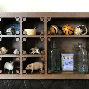 May include: A wooden shelf unit with nine compartments, featuring various decorative items, including dried fruit, glass bottles, a small pig figurine, a small sheep figurine, and a tin box with the text "Leone Violet" on it.