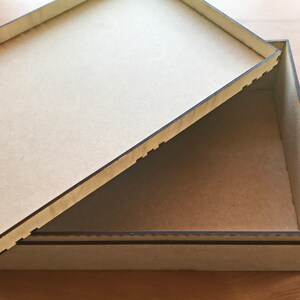May include: A wooden box with a lid that is open. The box is made of light brown wood and has a dark brown border. The lid is also made of light brown wood and has a dark brown border.