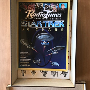 May include: A vintage Radio Times magazine cover featuring Star Trek: 30 Years. The cover features a blue background with a yellow border and a collage of images from the Star Trek franchise. The text "Radio Times" is in white with a yellow outline. The text "Star Trek" is in white with a red outline. The text "30 Years" is in white with a black outline. The cover also includes the text "100 Influential People in Star Trek", "Leonard Nimoy Looks Back", "Over 400 Episode and Film Descriptions", "Special First Ever Pull-Out Map of Federation Space".
