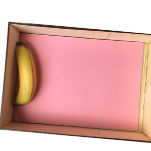 May include: A single yellow banana in a wooden box with a pink interior.