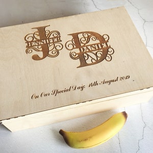 May include: A wooden box with a personalized inscription. The inscription reads "On Our Special Day: 4th August 2019" and features the initials "J" and "D" with the names "Jennifer" and "Daniel" incorporated into the letters.