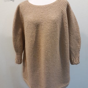 May include: A tan knitted sweater with a loose fit and long sleeves. The sweater has a waffle knit texture.