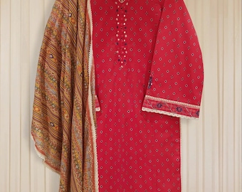 May include: A red and white patterned cotton kurta with a matching dupatta. The kurta has a V-neckline and is decorated with white lace trim and small mirror embellishments. The dupatta is a light brown and gold patterned fabric.