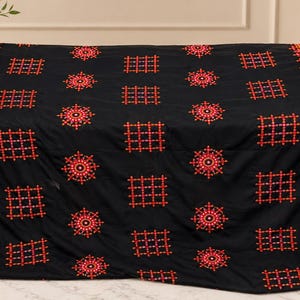 May include: A black fabric textile featuring a repeating pattern of embroidered red and orange square grids and circular floral motifs. The edges are finished with a wide, decorative border in shades of red, orange, and yellow.