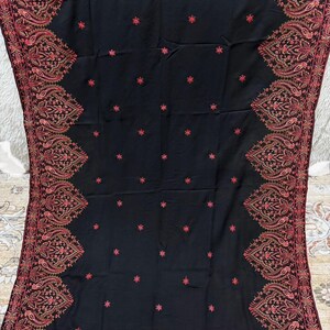 May include: Black shawl with intricate embroidery in shades of red and brown. The shawl features a detailed border design and scattered floral accents. A luxurious textile for warmth and style.