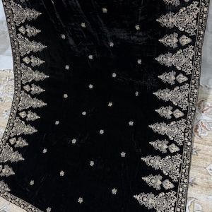 May include: A black velvet shawl with intricate gold embroidery along the edges and scattered across the surface. The ornate design features floral and paisley motifs, creating a luxurious and elegant appearance.