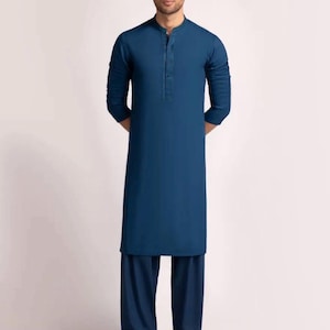 May include: A teal-colored, long-sleeved tunic and matching trousers. The tunic has a mandarin collar and a button-down placket. The trousers are loose-fitting. The outfit is worn with brown sandals. The background is plain white.