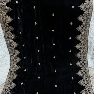 May include: A black velvet shawl with intricate gold embroidery along the edges and scattered across the surface. The design features floral and geometric patterns, creating a luxurious and elegant look. The shawl is likely made of a soft, flowing fabric.