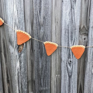 May include: A string of crocheted pumpkin pie slices in orange and yellow hangs against a weathered wood background.
