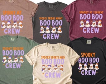 May include: Six short-sleeve crew neck t-shirts in various colors including mauve, charcoal, maroon, sage green, cream, and black. Each shirt features a graphic of four ghosts wearing hats and scarves with the text "BOO BOO CREW" and specific titles.