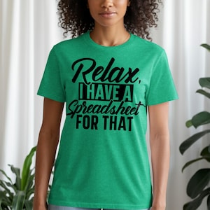 May include: A green t-shirt with the text "Relax, I have a Spreadsheet FOR THAT" in black. The shirt is a crew neck style and is being worn by a person. The background includes a white curtain and green plants.