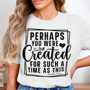 Op de afbeelding: Wit T-shirt met de tekst "PERHAPS YOU WERE CREATED FOR SUCH A TIME AS THIS" in zwart script. Het ontwerp bevat hart- en bladaccenten, met het bijbelvers Esther 4:14.