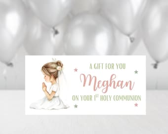 May include: A white rectangular card with the text "A GIFT FOR YOU Meghan ON YOUR 1ST HOLY COMMUNION" in green and pink. An illustration of a girl in a white dress with a veil is on the left side of the card. White balloons are in the background.
