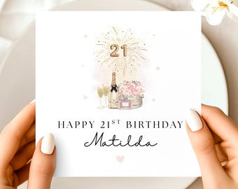 May include: A white birthday card with the text "Happy 21st Birthday Matilda". The card features a gold firework design with the number 21, a champagne bottle, two glasses, and a bouquet of pink flowers.