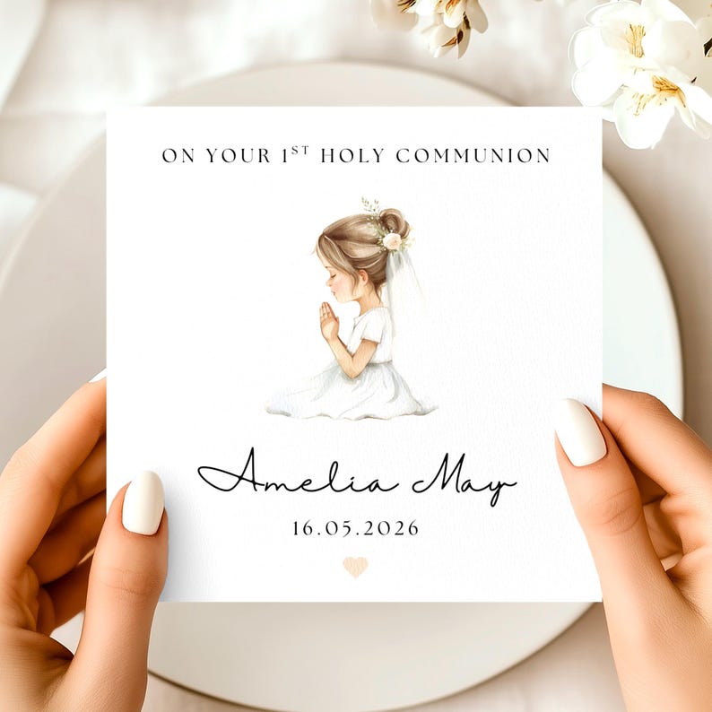 May include: A white card with the text "ON YOUR 1ST HOLY COMMUNION" and the name "Amelia May" in cursive. A watercolor illustration of a girl in a white dress praying is featured. The date "16.05.2026" is also included.