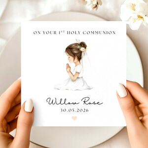 May include: A white card with the text "ON YOUR 1ST HOLY COMMUNION" and the name "Willow Rose" with the date "30.05.2026". The card features an illustration of a girl in a white dress with her hands clasped in prayer.