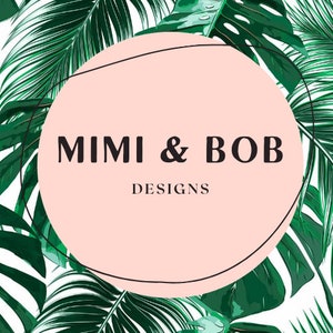 May include: A logo design featuring the text "MIMI & BOB DESIGNS" in a black font, set within a light pink circle. The circle is framed by a thin black line and surrounded by a background of lush green tropical leaves.