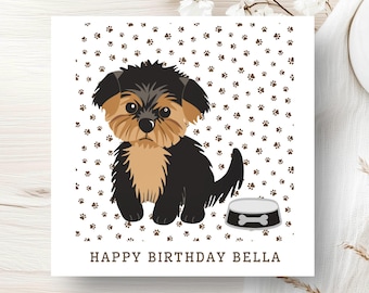 Può includere: Un biglietto d'auguri quadrato con l'illustrazione a cartone animato di un cucciolo nero e marrone seduto accanto a una ciotola grigia. Lo sfondo è bianco con un motivo di piccole impronte marroni. Il testo HAPPY BIRTHDAY BELLA è in marrone.