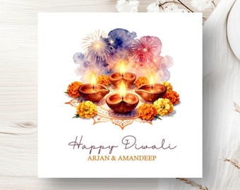 May include: A square greeting card featuring a watercolor illustration of four lit clay diya lamps surrounded by orange marigold flowers and a purple and blue firework background. The text reads Happy Diwali and ARJAN & AMANDEEP in dark script.