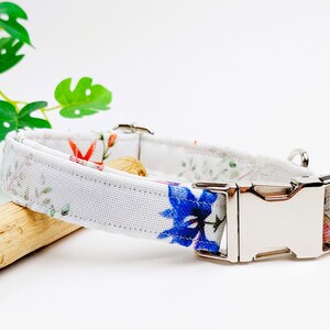 May include: White dog collar with a floral print featuring blue, red, and green flowers. The collar has a silver buckle.