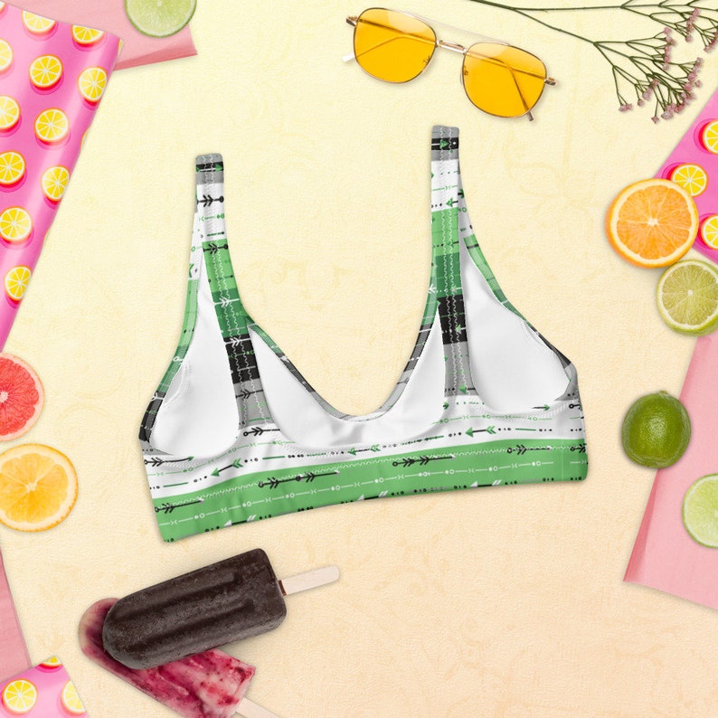 May include: Green and black striped bikini top with a white background and black arrow designs. The top has a scoop neck and adjustable straps.