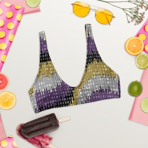 May include: A black, purple and gold bikini top with a binary code pattern. The top has a scoop neck and adjustable straps.