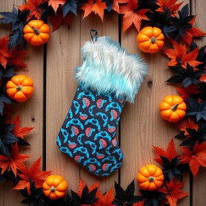 May include: A festive Christmas stocking with a Halloween theme. The stocking features a pattern of blue and red brains on a black background, with white and blue faux fur trim. The image includes orange pumpkins and autumn leaves.