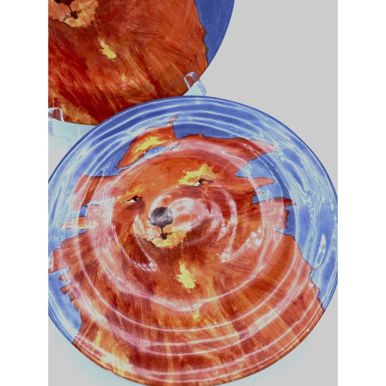 Pode incluir: Dois pratos decorativos com um design de urso. O urso &eacute; retratado em tons de castanho e laranja, rodeado por uma borda azul. Os pratos t&ecirc;m um estilo art&iacute;stico &uacute;nico, perfeitos para adicionar um toque de fantasia a qualquer mesa.