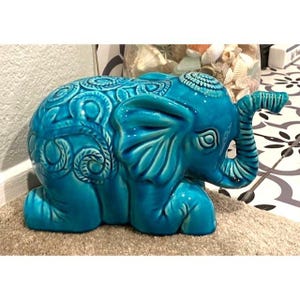 May include: A turquoise ceramic elephant figurine with intricate swirling patterns on its body. The elephant is sitting with its trunk raised and its ears spread out.