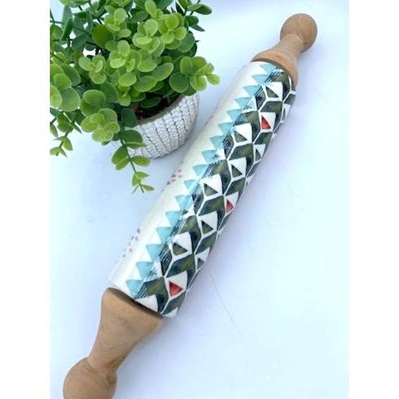 May include: A wooden rolling pin with a white, blue, and red geometric pattern. The rolling pin is approximately 15 inches long.