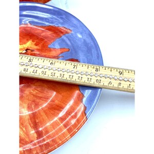 Pode incluir: Um prato decorativo com um desenho floral vermelho e laranja sobre um fundo azul. Um colar de corrente prateada &eacute; medido com uma r&eacute;gua. O colar tem aproximadamente 18 cm de comprimento.