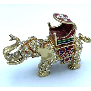 May include: A gold-colored elephant figurine with a jeweled howdah on its back. The elephant is decorated with colorful enamel and rhinestones. The howdah is red with green and blue accents.