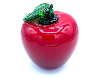 May include: A red glass apple with a green glass leaf on top. The apple is shiny and has a smooth surface.