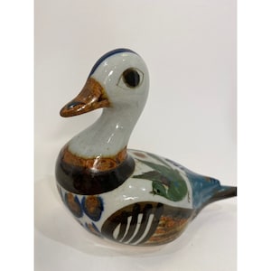May include: A ceramic duck figurine with a white body, brown and blue accents, and a green and blue tail. The duck has a brown beak and black eyes.