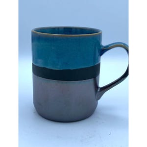 May include: A ceramic mug with a teal blue glaze, a black stripe, and a iridescent purple glaze. The mug has a rounded handle.