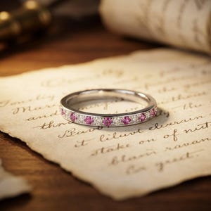 Può includere: Un anello a fascia color argento caratterizzato da un motivo alternato di piccole pietre preziose rotonde di un rosa vivace e pietre bianche chiare e scintillanti, incastonate lungo l'intera circonferenza esterna in un design simmetrico.