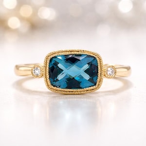 May include: A gold ring featuring a large, rectangular, teal-colored gemstone with a cross-like pattern. The ring has a detailed, textured bezel setting and small accent diamonds on each side of the main stone. The band is smooth and polished.