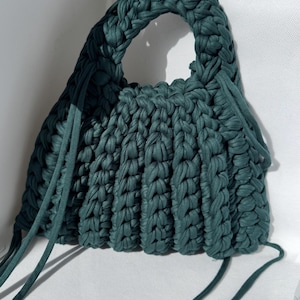 May include: A teal green crocheted tote bag with a single handle and long ties.