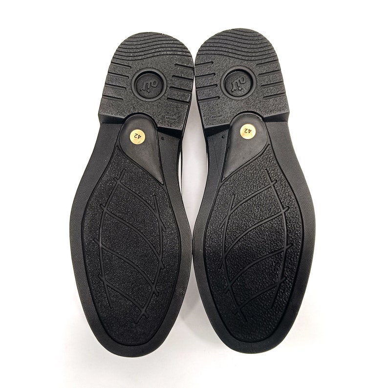 May include: A pair of black leather shoes with a textured sole. The soles are marked with the size 42.