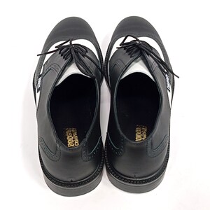 May include: A pair of black leather shoes with white accents. The shoes have a lace-up closure and a wingtip design. The shoes are made by the "Converse" company.