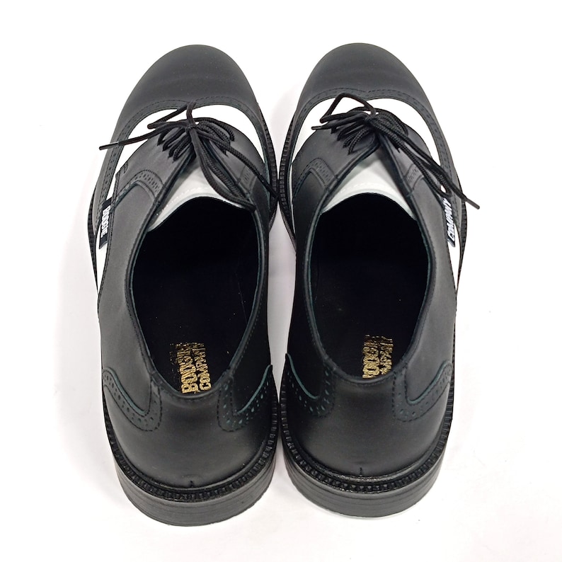 May include: A pair of black leather shoes with white accents. The shoes have a lace-up closure and a wingtip design. The shoes are made by the "Converse" company.