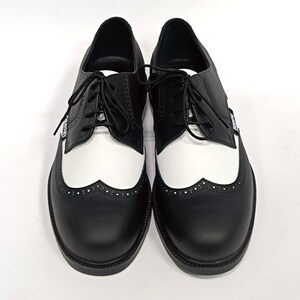 May include: A pair of black and white leather shoes with a wingtip design and a lace-up closure.